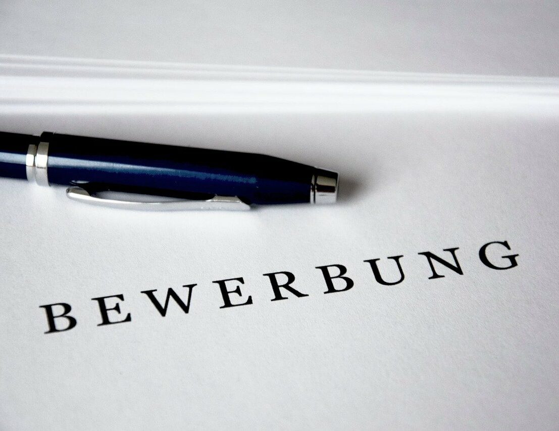 Weißes Blatt mit einem Stift und darauf steht das Wort Bewerbung